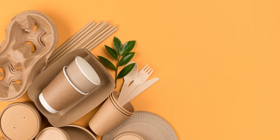 Kraft paper food utensils, paper containers and cups, drinking straws on orange background with copy space
