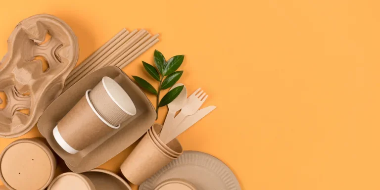 Kraft paper food utensils, paper containers and cups, drinking straws on orange background with copy space