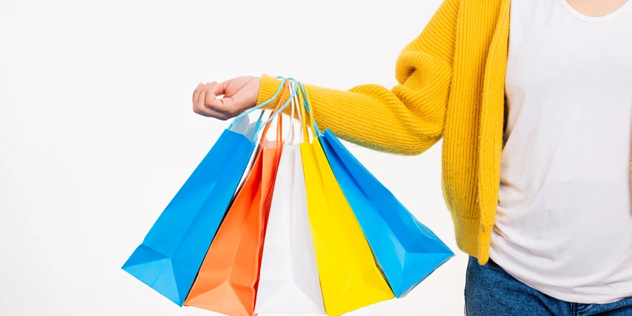 Woman hand she wears yellow shirt holding shopping bags multicolor