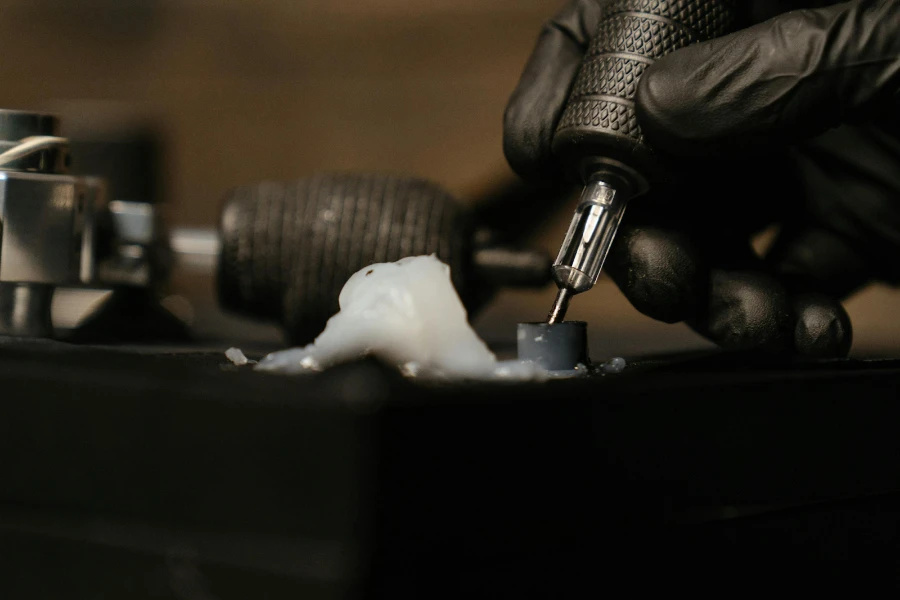Black-gloved hand dipping tattoo gun in ink