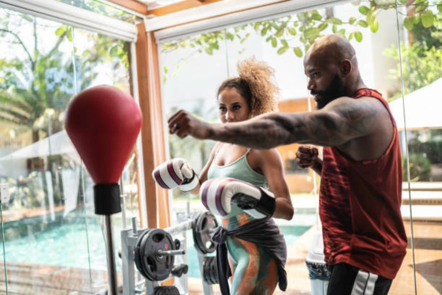 Тренер по боксу тренирует женщину в домашнем спортзале