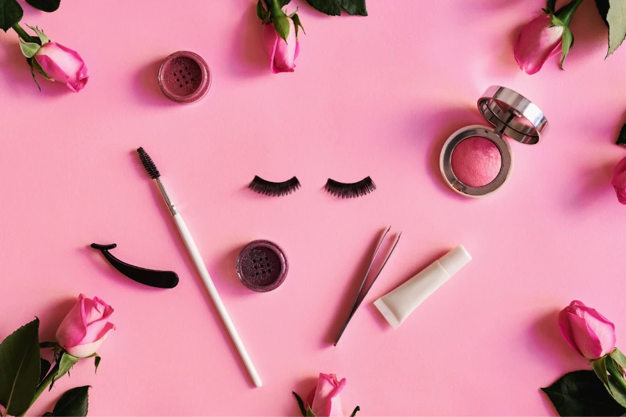 Pegamento para pestañas y otras herramientas de belleza sobre una mesa rosa