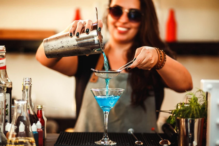 Barman féminin versant un verre à travers une passoire à cocktail
