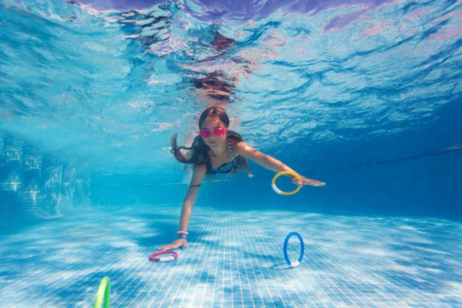 Niña buceando en la piscina para alcanzar anillos de piscina con peso