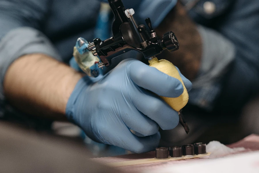 Behandschuhter Künstler, der eine Tätowierpistole mit bequemem Griff verwendet