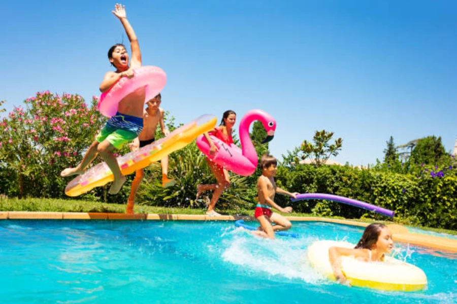 Niños saltando en la piscina al aire libre con varios juguetes inflables para la piscina