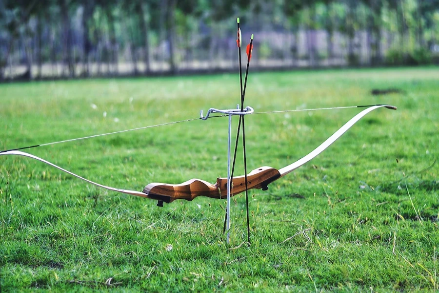 Longbow on grass with arrows on ground beside it