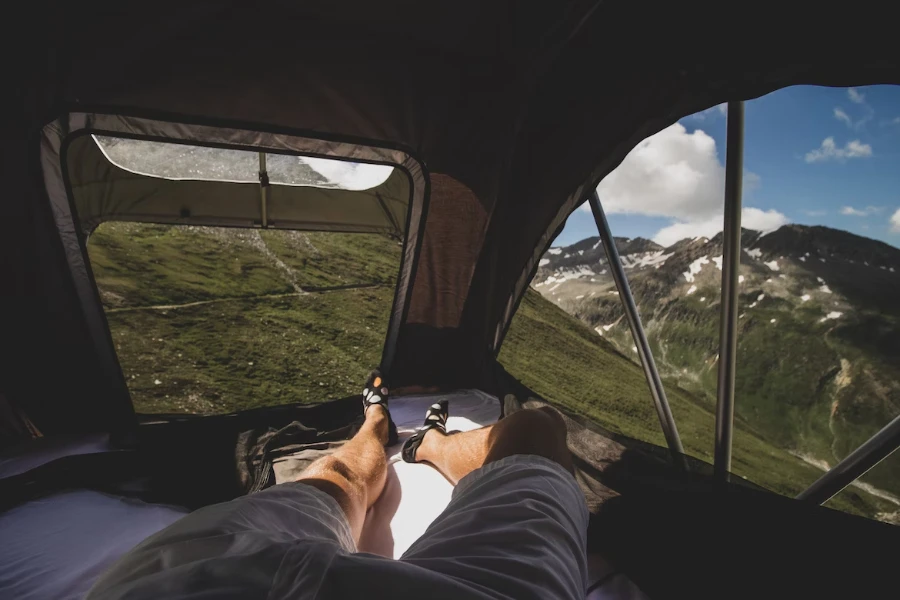 Man lying down in rooftop tent with mountain views