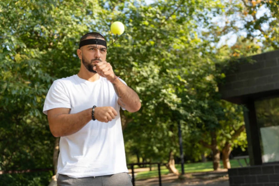 Мужчина бьет боксерский рефлекторный мяч в открытом парке