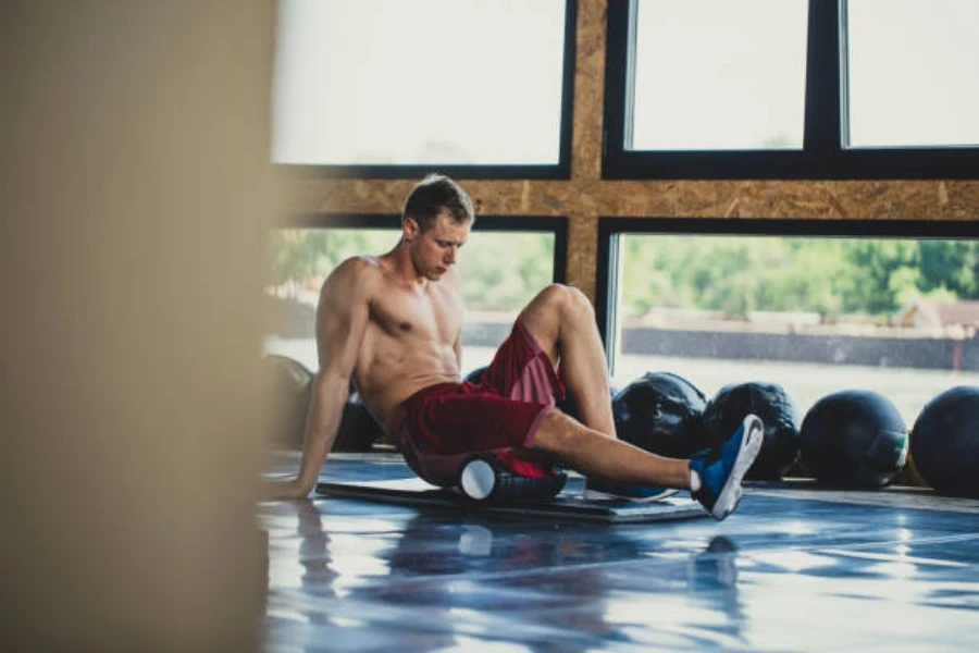 Uomo che utilizza un rullo di schiuma nera nello spazio della palestra