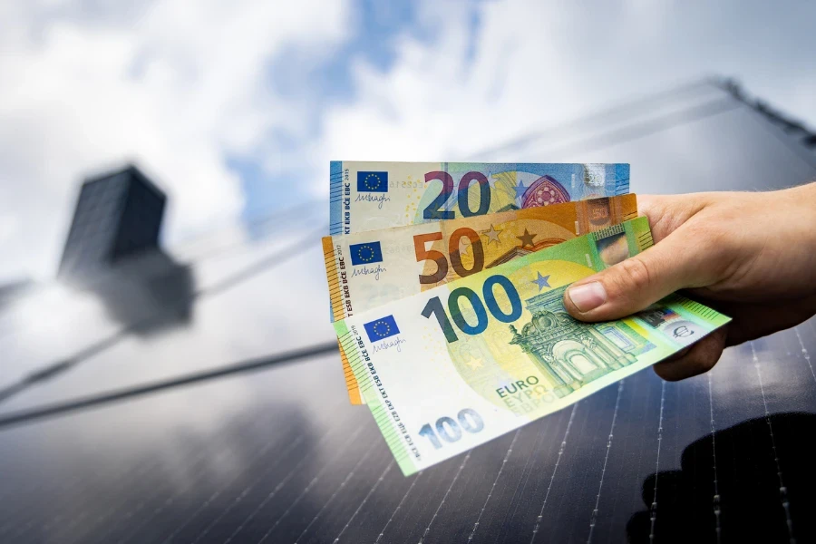 Eine Hand hält das Geld neben dem Solarpanel