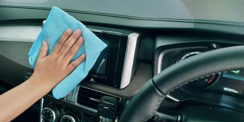 Persona limpiando el salpicadero de un coche con un paño de microfibra
