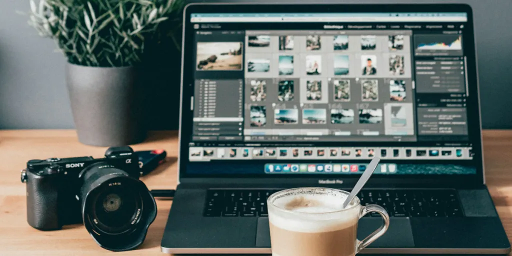 Programa de edição de fotos aberto em um laptop com câmera ao lado e café na frente
