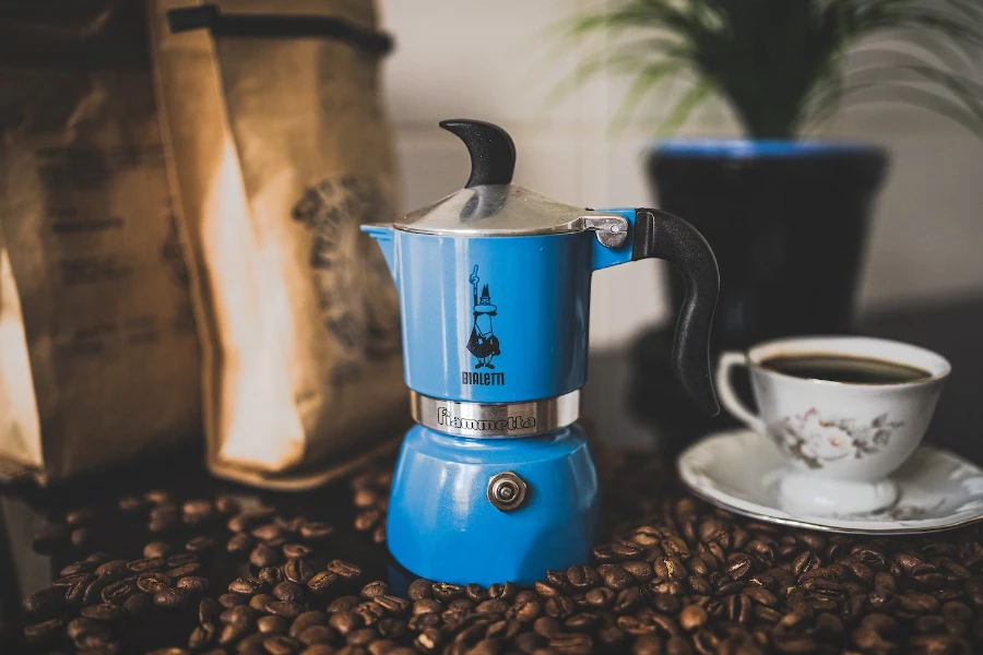 Small blue moka pot and cup and saucer on a bed of coffee beans