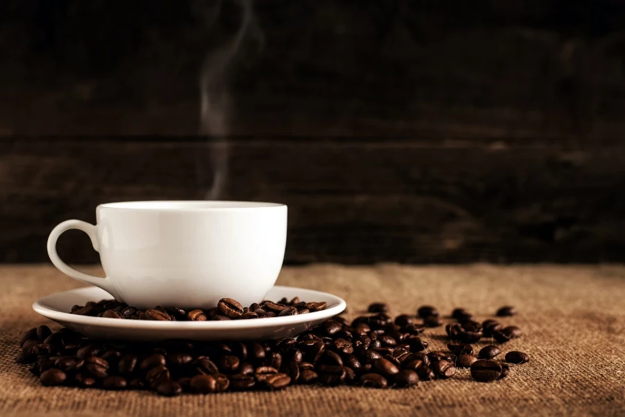 コーヒー豆の上の白いカップのコーヒーから出る蒸気