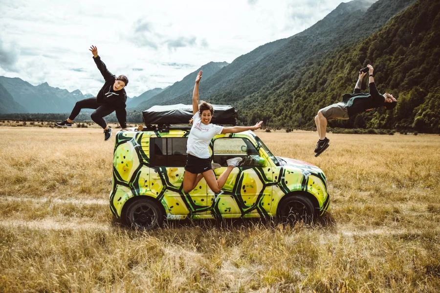 ثلاثة أشخاص يقفزون أمام السيارة مع خيمة على السطح