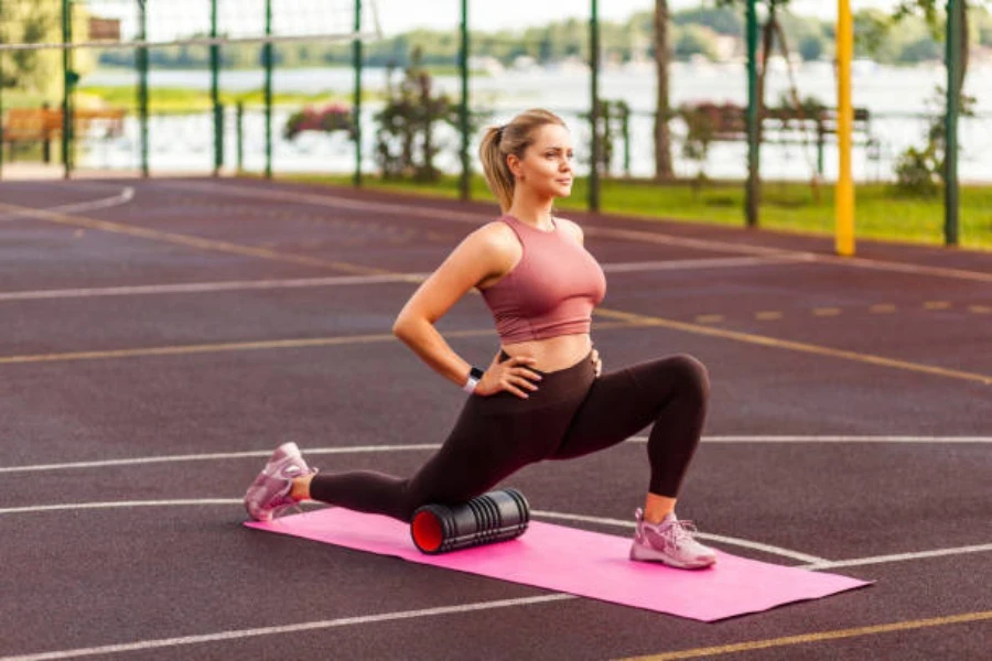 Mulher se alongando na pista de corrida usando rolo de espuma preta