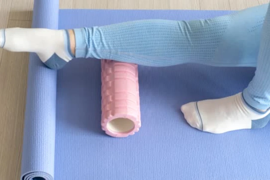 Femme utilisant un rouleau en mousse à grille rose bébé sur un tapis de yoga