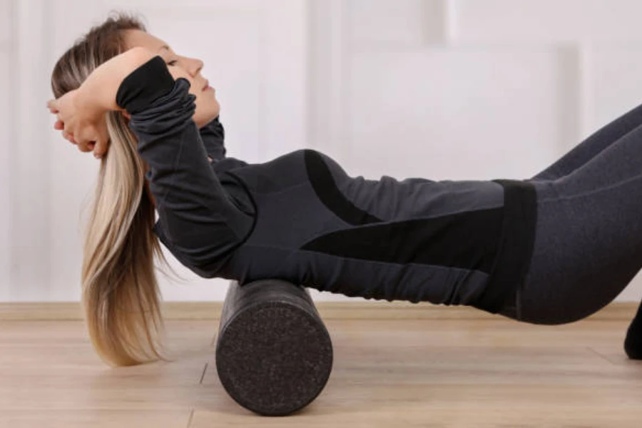 Woman using black soft foam roller on her upper back