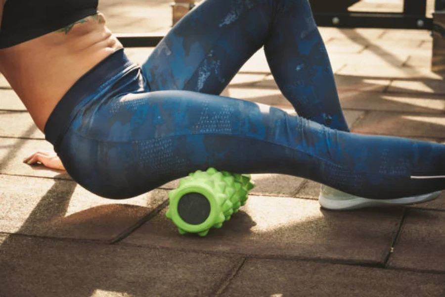 Woman using green deep tissue foam roller outside