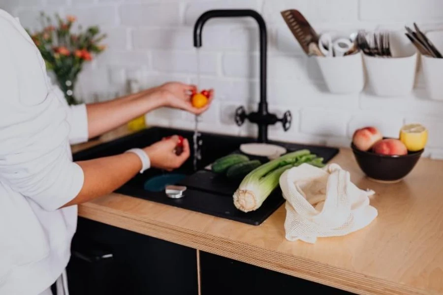 Mulher lavando legumes na pia da cozinha preta