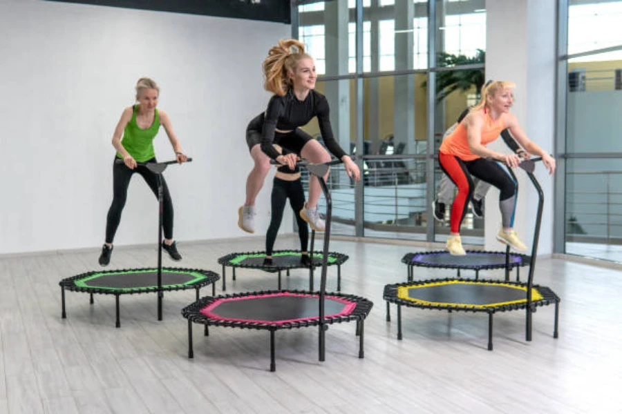 Women in fitness class jumping on trampolines with handles