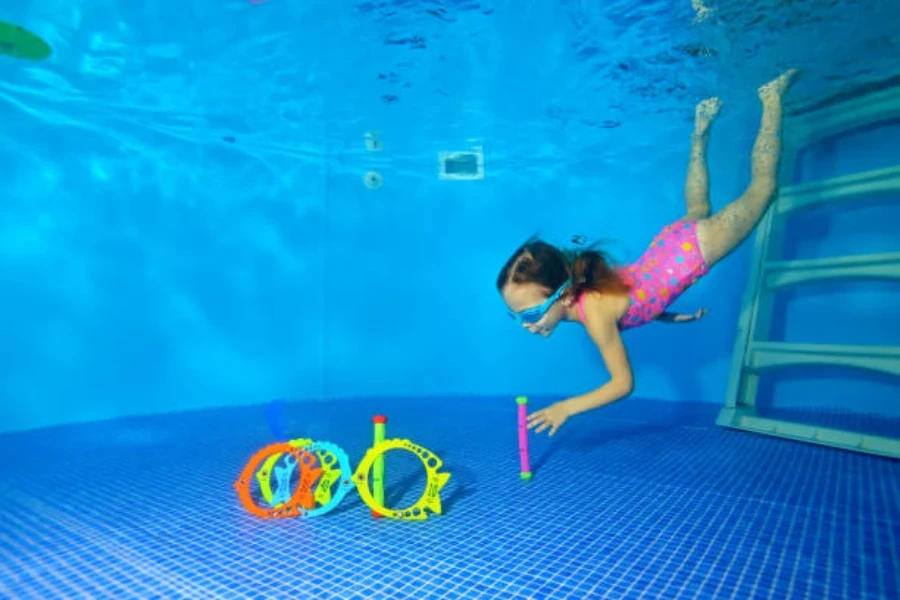 Niña buceando hasta el fondo de la piscina en busca de juguetes de buceo