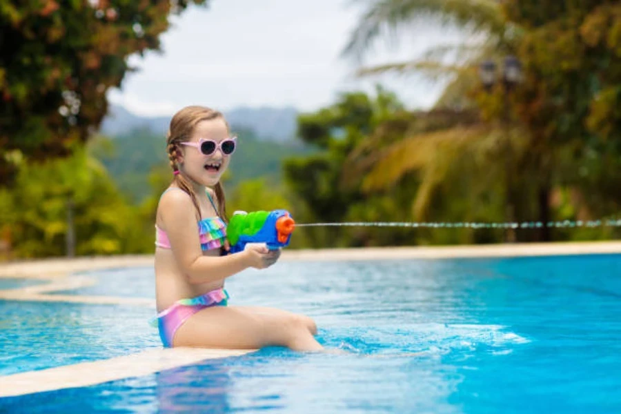 Ragazza che si siede sul lato della piscina con la pistola ad acqua