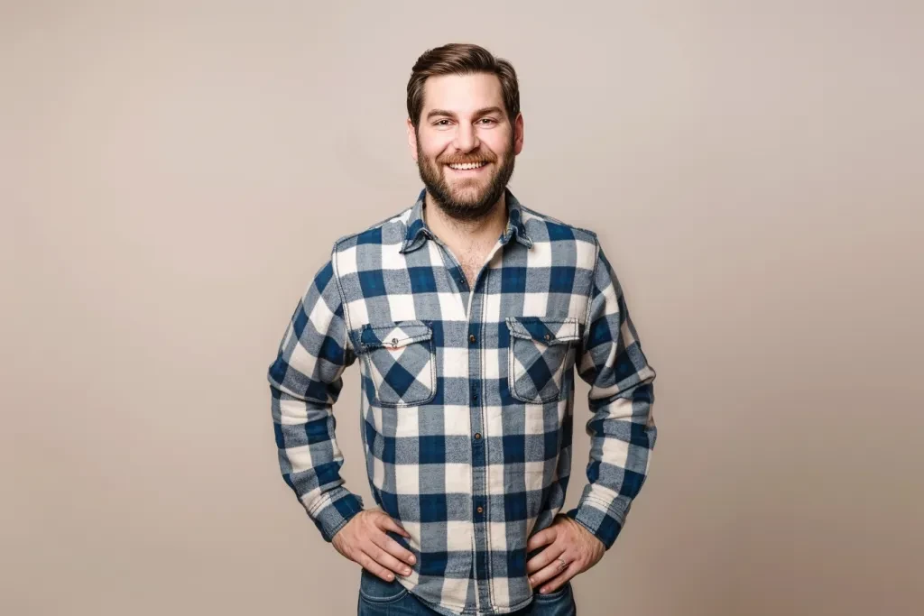 A handsome man wearing a blue and white plaid shirt with jeans