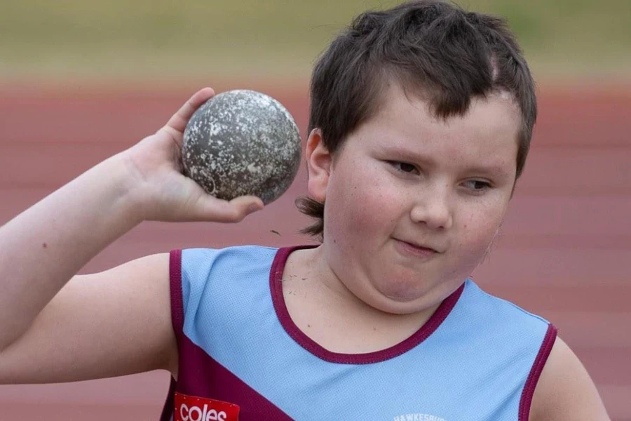 Un bambino con in mano una palla da allenamento per il lancio del peso