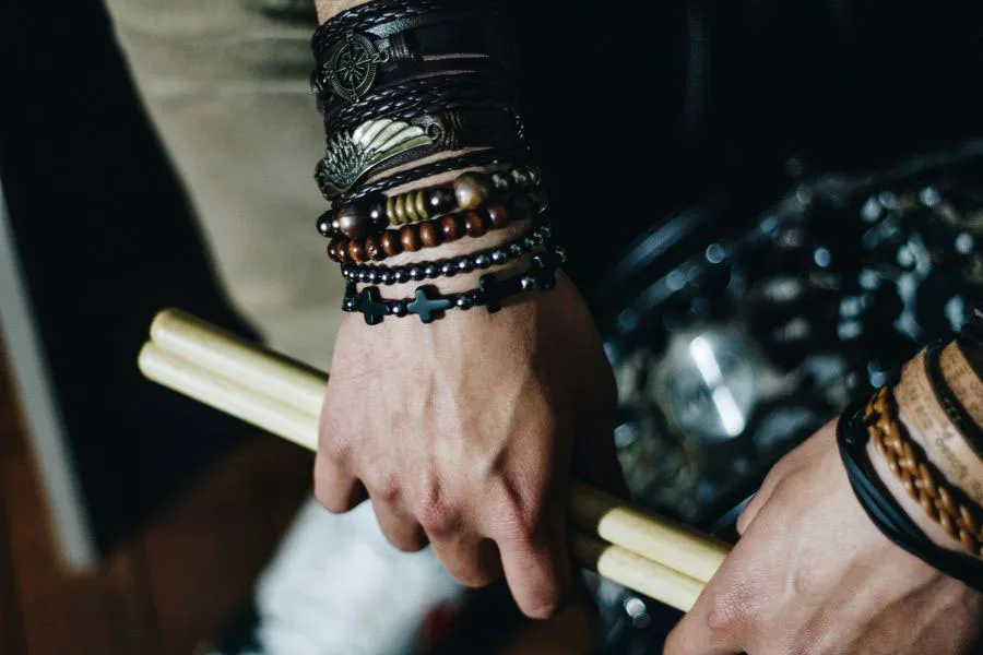 Sebuah tangan dengan gelang bertumpuk bertekstur berbeda memegang stik drum