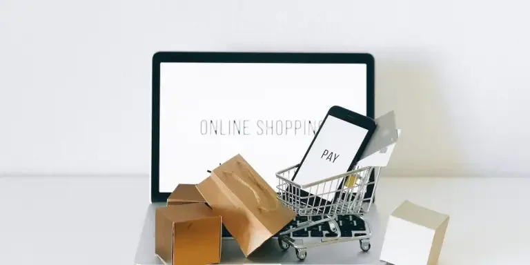 A laptop with a miniature shopping cart and shopping bags