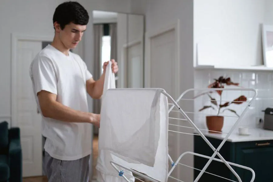 A man hanging up clothes on a clothes drying rack