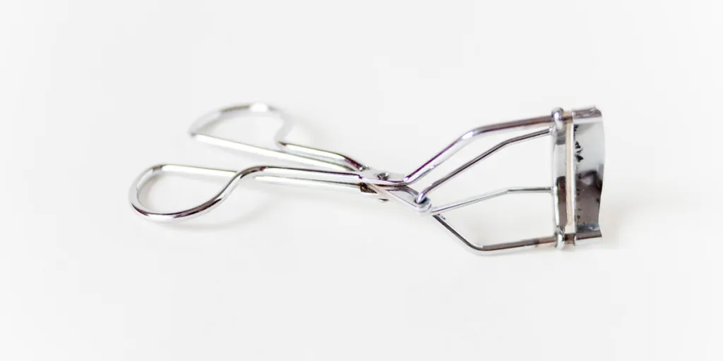 A metal eyelash curler on a white background