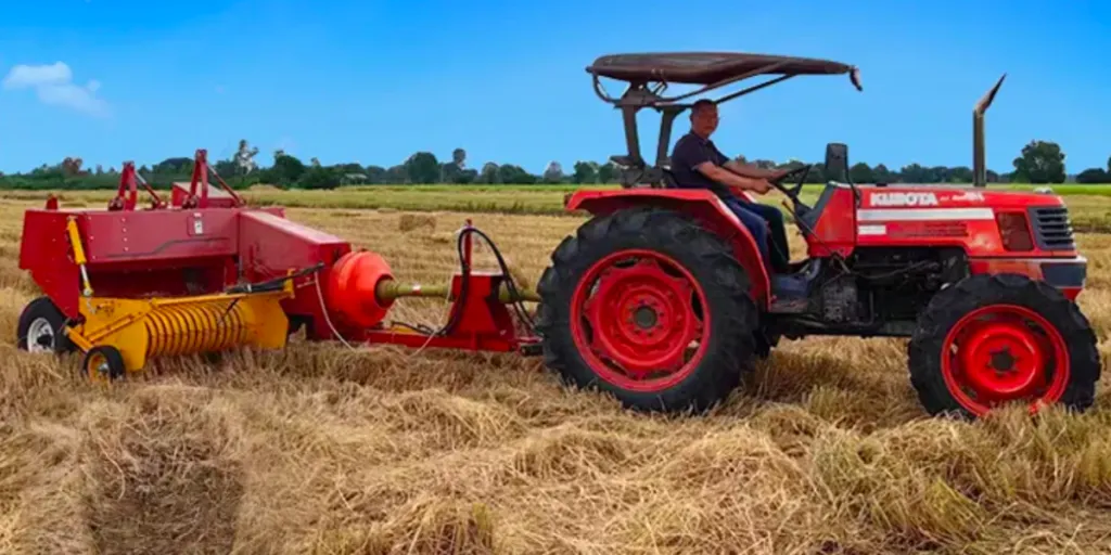 A square hay baler at work, being towed by a tractor