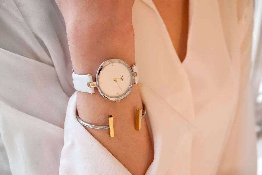 Seorang wanita dengan blus putih menumpuk jam tangan dengan gelang terbuka