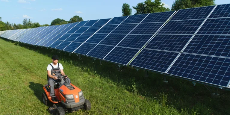 A worker on a garden tractor mows grass on a solar panel farm