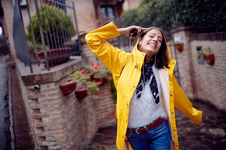 Una joven con un impermeable amarillo en un paseo por la calle mientras disfruta de la música