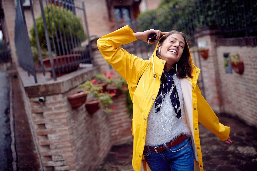 Uma jovem com uma capa de chuva amarela caminhando pela rua enquanto ouve música