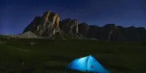 An illuminated blue tent in a valley