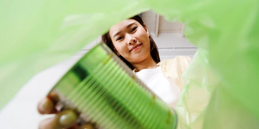 Asiatische Frau bringt und sortiert Plastik-Aluminiumdosen in den Recyclingbehälter POV