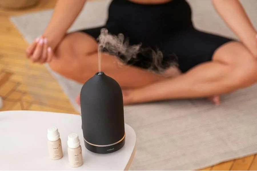 Black oil diffuser in front of woman doing yoga
