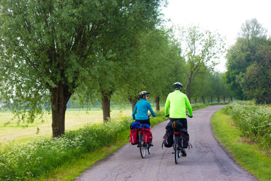 Pasangan bersepeda di sepanjang jalan yang ditumbuhi pepohonan dengan tas keranjang beban