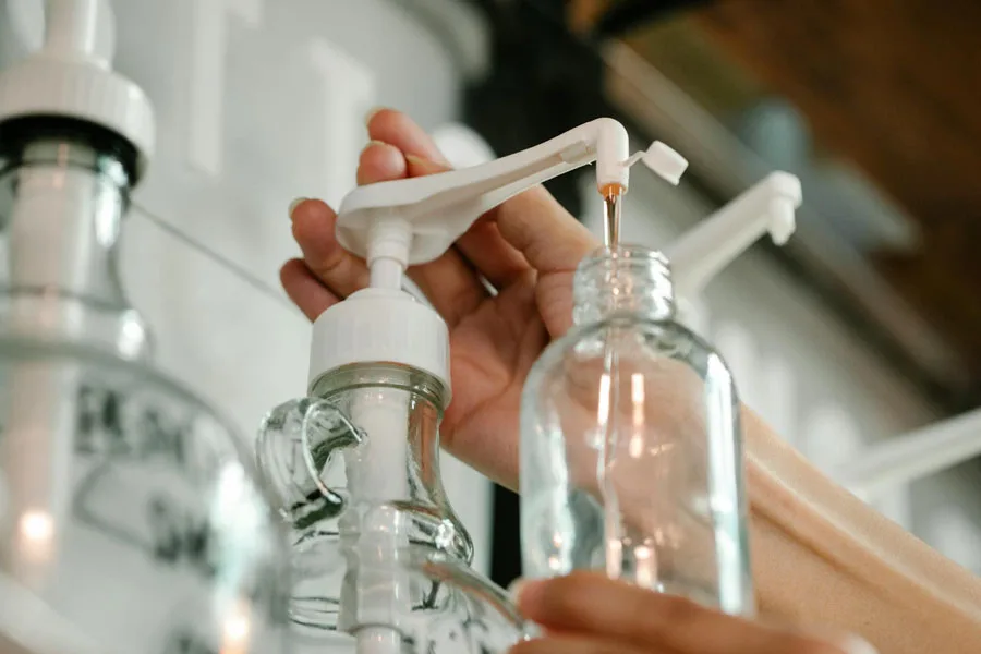 Crop unrecognizable person pushing and pouring soap from dispenser to plastic bottle