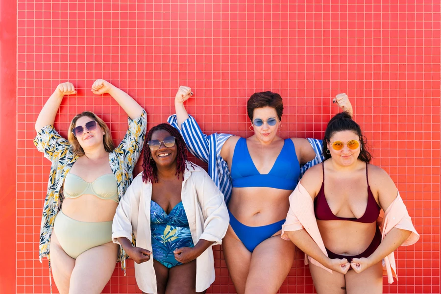 Grupo diversificado de mulheres vestindo trajes de banho e flexionando