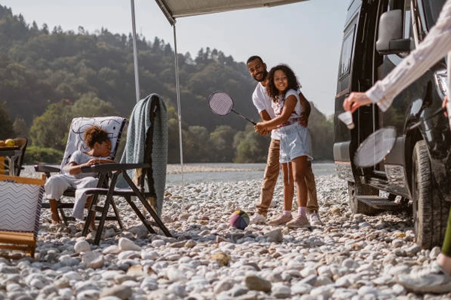 Family using badminton set to play next to camper van