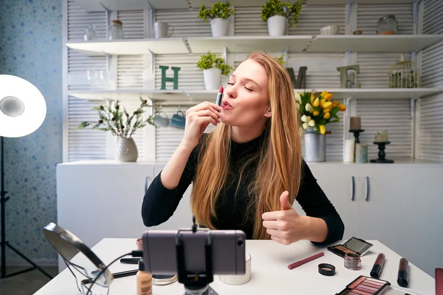 Female vlogger applying lipstick while filming