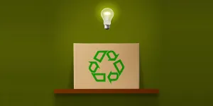 Glowing light bulb in mid-air over the cardboard box with green recycling symbol on wooden shelf