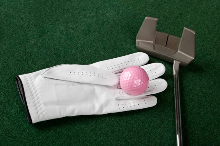 Golf glove, pink ball, and putter lying on putting green