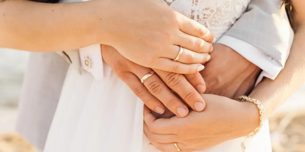 Mãos de uma noiva e um noivo usando alianças de casamento